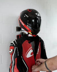 Person hanging a red and black motorcycle helmet and jacket on the wall-mounted rack against a white tiled wall.